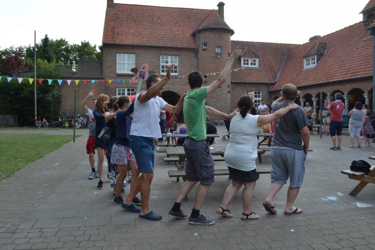 groep volwassenen en kinderen die op binnenplaats van een gebouw in een cirkelvormige polonaise dansen